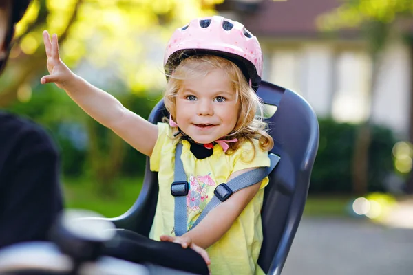 Retrato de menina pequena criança com capacete de segurança na cabeça sentado no assento da bicicleta dos pais. Rapaz de bicicleta no fundo. Conceito de proteção segura e infantil. Família e fim de semana viagem atividade. — Fotografia de Stock