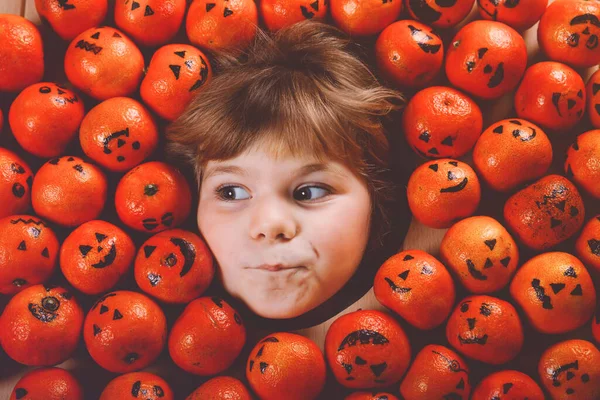 Grappig portret van een schattig peutermeisje met oranje mandarijn die eruit ziet als kleine pompoenen. Vrolijk glimlachend kinderfeest Halloween festival of feest. Briefkaarten maken voor vrienden. — Stockfoto