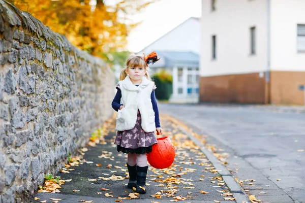 魔女のトリックやハロウィンの扱いに身を包んだ小さな幼児の女の子。幸せな子供は屋外で、オレンジ面白い帽子とカボチャの袋で甘い出没します。10月のファミリーフェスティバルシーズン。野外活動 — ストック写真