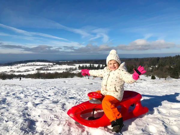 活泼的蹒跚学步的小女孩骑着雪橇滑下山，可爱的小女孩在冬天坐在雪橇上在户外玩得很开心。健康兴奋的孩子滑雪下坡，家人过冬. — 图库照片