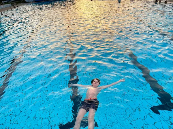 Niño de la escuela salpicando en una piscina al aire libre en el cálido día de verano. Feliz niño preadolescente saludable disfrutando de un clima soleado en la piscina pública de la ciudad. Actividad infantil al aire libre con agua. — Foto de Stock