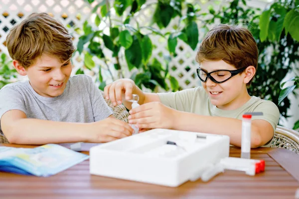 Due ragazzi che fanno esperimenti chimici in laboratorio a scuola. I bambini con occhiali protettivi studiano utilizzando pipette che rilasciano liquido in provetta, caucasico, biochimica. classe di chimica. — Foto Stock