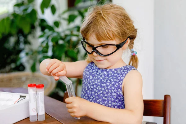 Маленькая дошкольница проводит химический эксперимент в лаборатории в школе. Тоддлер ребенок в защитных очках исследования капли жидкости для проверки трубки, кавказский, биохимия. класс химии. — стоковое фото