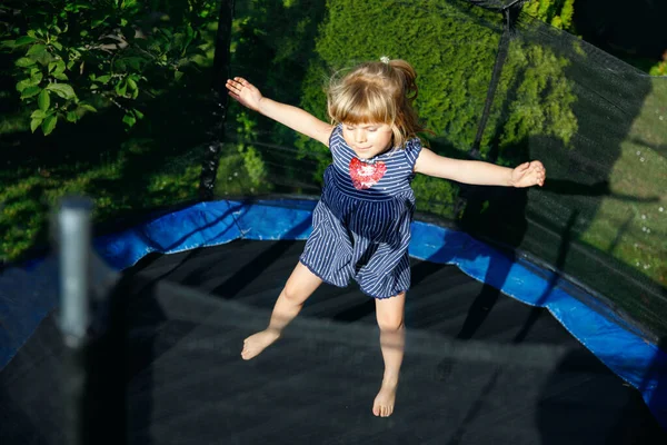 Uma miúda pré-escolar a saltar em trampolim. Criança engraçada feliz se divertindo com a atividade ao ar livre no verão. Esportes e exercícios para crianças. — Fotografia de Stock