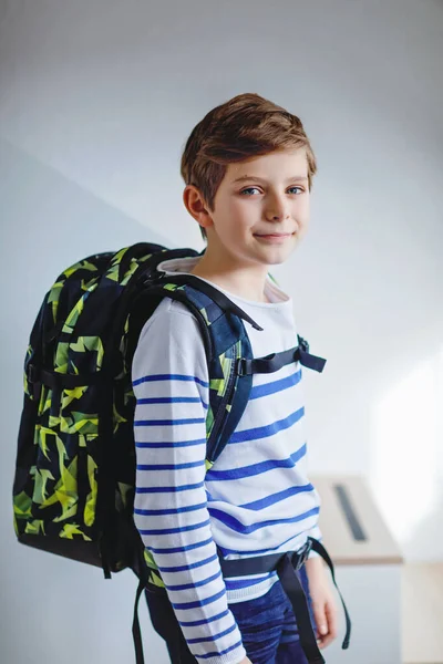 Okul çantalı güzel çocuk sabahın erken saatlerinde odada duruyor. Okula ve derslere giden mutlu sağlıklı çocuk. Eğitim kavramı