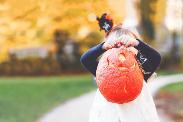 Malá batolátko dívka oblečená jako čarodějnice trik nebo dárek na Halloween. Šťastné dítě venku, s pomerančovou legrační čepicí a dýňovou taškou na sladké strašení. Rodinná sezóna v říjnu. Nerozpoznatelná tvář — Stock fotografie