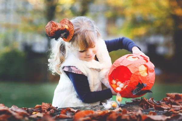 Маленькая девочка, одетая как ведьмин трюк или угощение на Хэллоуин. Счастливый ребенок на улице, в оранжевой веселой шляпе и мешке для сладкого. Сезон семейных фестивалей в октябре. Активность на открытом воздухе — стоковое фото