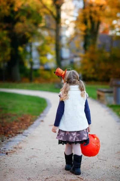 Niña pequeña vestida como un truco de bruja o trato en Halloween. Niño feliz al aire libre, con sombrero divertido naranja y bolsa de calabaza para dulce refugio. Temporada familiar en octubre. Cara irreconocible —  Fotos de Stock