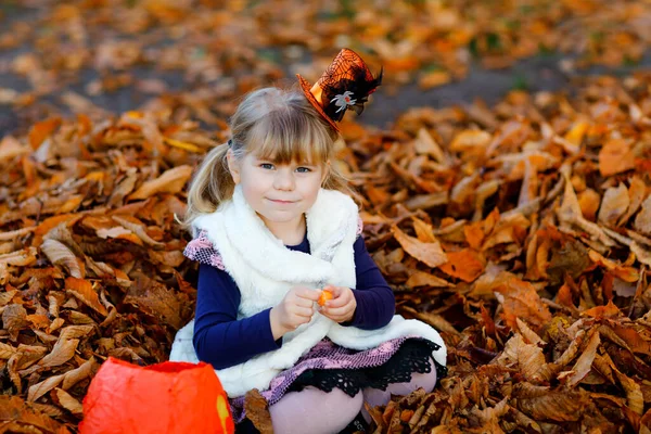 Niña pequeña vestida como un truco de bruja o trato en Halloween. Niño feliz al aire libre, con sombrero divertido naranja y bolsa de calabaza para dulce refugio. Temporada de festivales familiares en octubre. Actividades al aire libre —  Fotos de Stock