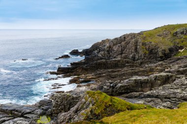 Malin Head, Donegal, İrlanda 'da engebeli bir manzara. Kayalıkları olan dalgalı bir sahil, sisli bulutlu bir günde koyunlu yeşil kayalık bir arazi..