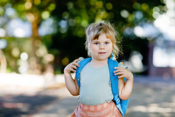 彼女の最初の日にかわいいかわいい幼児の女の子は学校に行く。保育園や幼稚園まで歩く健康な美しい赤ちゃん。街の通りのバックパックを持つ幸せな子供、屋外. — ストック写真