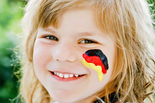 Niña rubia en edad preescolar viendo el partido de fútbol en público. Feliz alegre niño emocionado acerca de ganar el partido de partido de la selección de fútbol nacional favorita. chica con bandera alemana en la cara. —  Fotos de Stock