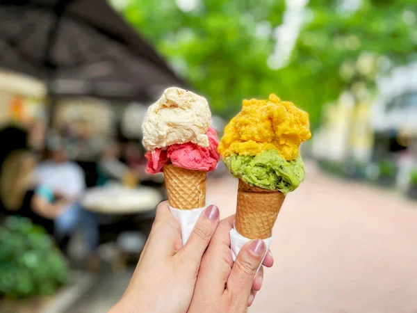 Jeune femme mains tenant des cônes de crème glacée le jour de l'été dans la ville. Savoureux fruits colorés et crème glacée aux baies — Photo