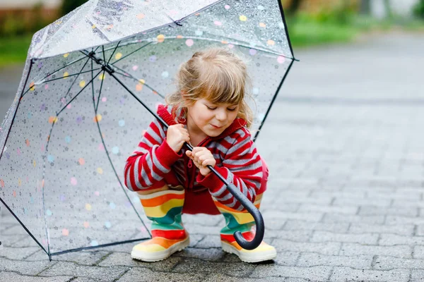 A kisbaba esős napokon nagy esernyővel játszik. Boldog pozitív gyermek fut az esőben, pocsolyák. Óvodás gyerek esőkabátban és gumicsizmában. Gyermekek aktivitása a rossz idő napján. — Stock Fotó