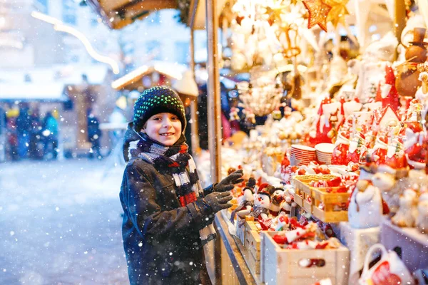 Kleiner süßer Junge bei der Dekoration auf dem Weihnachtsmarkt. Schöne Kindereinkäufe für Spielzeug und Dekorationsartikel für den Baum. Weihnachtsmarkt in Deutschland. — Stockfoto