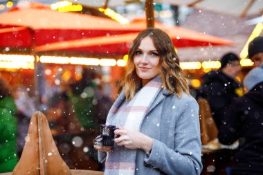 Güzel genç bir kadın sıcak punç içiyor, Alman Noel pazarında sıcak şarap içiyor. Kış kıyafetleri içinde mutlu bir kız. Arka planda ışıklar var. Berlin, Almanya 'da kış günü kar tatilinde..