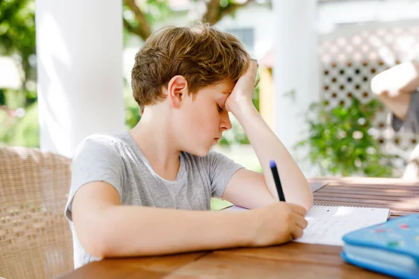 Hard-working sad school kid boy making homework during quarantine time from corona pandemic disease. Upset tired child on home schooling in coronavirus covid time, schools closed.