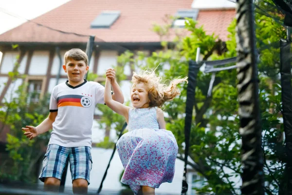 Little preschool girl and school kid boy jumping on trampoline. Happy funny siblings children having fun with outdoor activity in summer. Sports and exercises for kids. Family have fun. — Stock Photo, Image