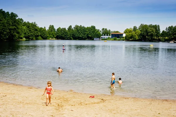 Mała blondyneczka bawiąca się pluskaniem w jeziorze w letni dzień, na świeżym powietrzu. Szczęśliwe dziecko uczy się pływać. Aktywny wypoczynek z dziećmi na wakacjach. Niebezpieczeństwo na jeziorach krajowych — Zdjęcie stockowe