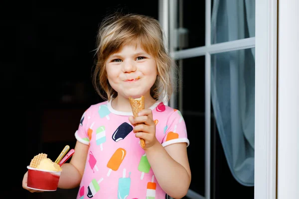 Cute funny preschool girl eating fruit ice cream at home. Happy healthy toddler child smiling and tasting ice-cream in waffle cone. Lovely kid enjoying summer dessert. — Stock Photo, Image