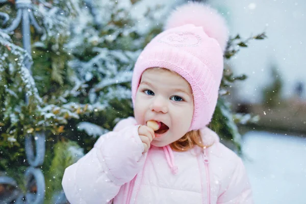 冬天在户外散步的小女孩的画像。可爱的幼儿吃甜棒棒糖.孩子们在寒冷的雪天玩得很开心.穿着保暖的婴儿粉红衣服，头戴有泡泡的帽子. — 图库照片