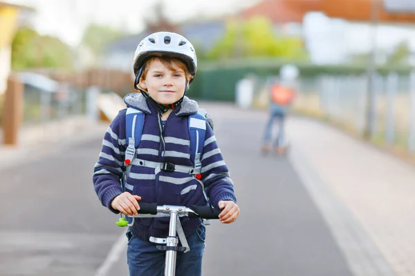 Kasklı aktif okul çocuğu güneşli bir günde şehirde scooterıyla geziyor. Renkli elbiseli mutlu çocuk okula giderken bisiklet sürüyor.. — Stok fotoğraf