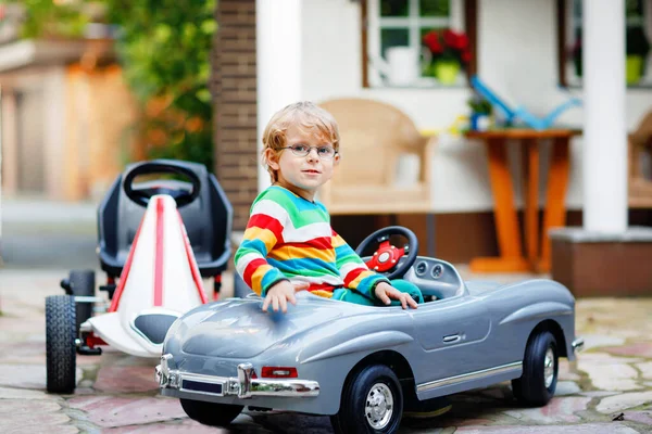 Piccolo bambino in età prescolare guida grande macchina giocattolo e divertirsi, all'aperto. Felice bambino giocare e avere attività all'aperto. Ragazzo con gli occhiali sorridente, azioni estive per i bambini — Foto Stock