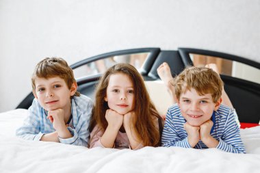 Pijamalı üç mutlu çocuk pijama partisini kutluyor. Anaokulu, okul çocukları ve gecelikli kız birlikte eğleniyorlar. Çocuklar yatakta birlikte oynuyorlar. Evde yastık savaşı yapmak..