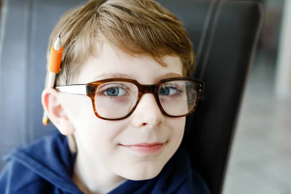 Portret van een leuk schooljongetje met een bril. Mooi gelukkig kind kijkend naar de camera. Schooljongen maakt grapjes met een pen, in de mond en achter het oor. Onderwijsconcept. — Stockfoto