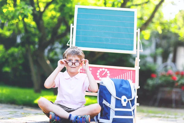 Szczęśliwy chłopczyk w okularach siedzący przy biurku, plecaku czy torbie. Uczeń z tradycyjną niemiecką torbą szkolną o nazwie Schultuete pierwszego dnia w szkole. Wracamy do szkoły. — Zdjęcie stockowe