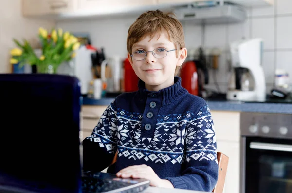 Junge mit Brille lernt zu Hause am Laptop für die Schule. Entzückendes Kind, das Hausaufgaben macht und Notizbuch und moderne Geräte benutzt. Heimschulkonzept. — Stockfoto