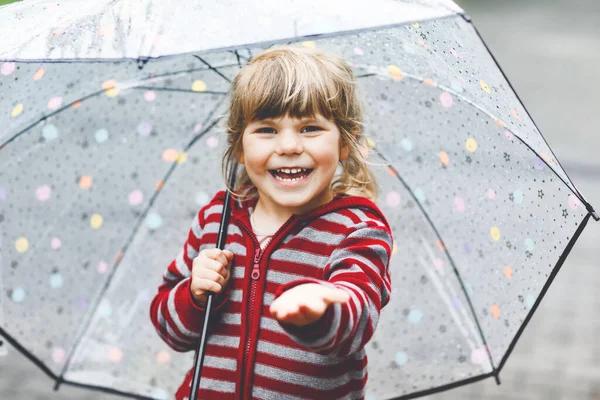 Little toddler girl playing with big umbrella on rainy day. Happy positive child running through rain, puddles. Preschool kid with rain clothes and rubber boots. Children activity on bad weather day. — Stock Photo, Image