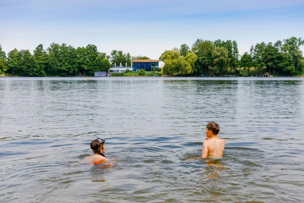 Dvě děti, školák a holka se baví cákáním v létě v jezeře, venku. Šťastné děti plavou. Aktivní volný čas s dětmi na dovolené. Nebezpečí na domácích jezerech. Letní aktivita — Stock fotografie