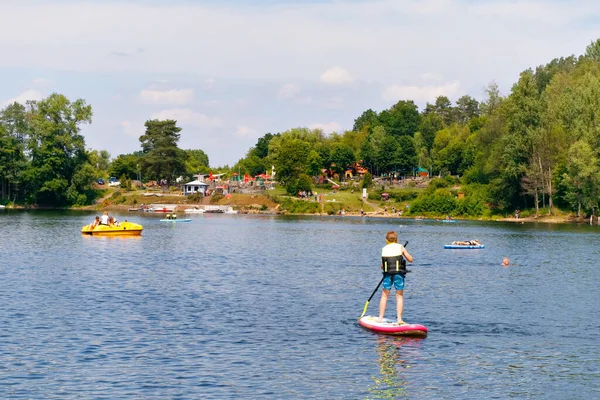 Junge paddelt auf Surfbrett auf einem See. Aktives Kind auf modernem, trendigem Stand Up Paddle Board. Sommerferienaktivität für Familie und Kinder. Aktivitäten im Wassersport. — Stockfoto