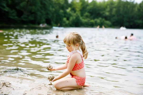 Pequena menina pré-escolar loira se divertindo com brincar com areia no lago no dia de verão, ao ar livre. Criança feliz aprendendo natação. Lazer ativo com crianças em férias. Perigo em lagos domésticos — Fotografia de Stock