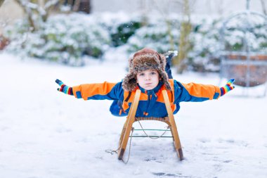 Küçük çocuk kar yağışı sırasında kızak sürmekten hoşlanıyor. Eski model kızakla gezen mutlu anaokulu çocuğu. Çocuk dışarıda karla oynuyor. Kışın aile Noel tatili için aktif eğlence