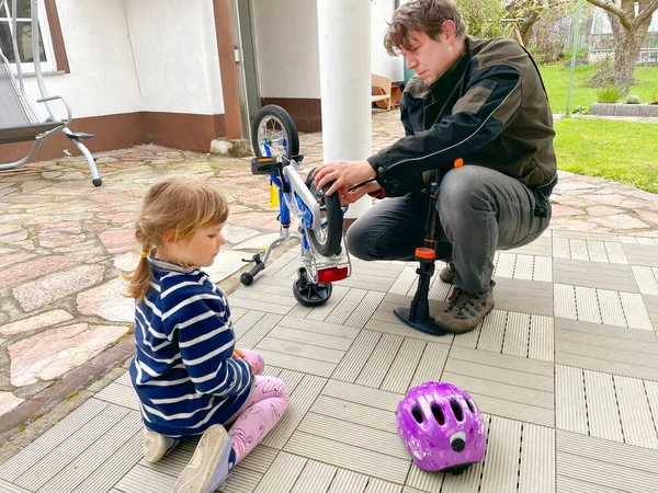 Mała przedszkolanka i ojciec naprawiają łańcuch na rowerze i pompują opony rowerowe. Dziecko i tata pracują razem. Rodzina na zewnątrz. Aktywny wypoczynek. Córka i tata spędzają czas. Maluch uczący się od człowieka — Zdjęcie stockowe