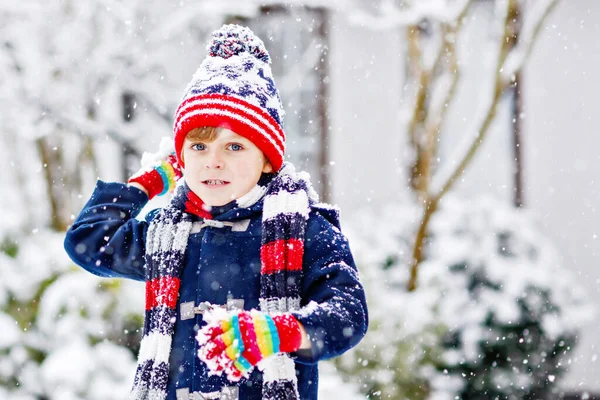 Engraçado menino em roupas coloridas jogando ao ar livre durante forte queda de neve — Fotografia de Stock