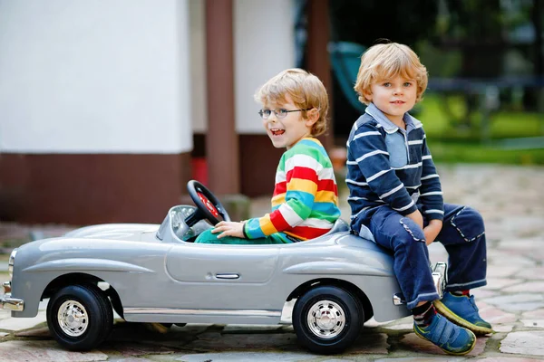 Dois meninos pré-escolares brincando com o carro de brinquedo velho grande no jardim de verão, ao ar livre. Crianças felizes brincam juntas, dirigindo carro. Atividade ao ar livre para crianças. Irmãos e amigos no dia quente — Fotografia de Stock