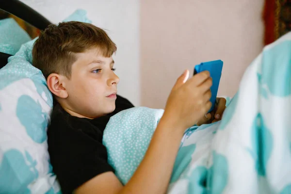 School kid boy reading an ebook at night. Adorable child in bed with interesting book. Portable reader holding by preteen boy. — Stock Photo, Image