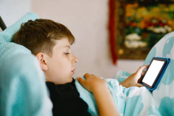 Skolgrabben läser en bok på nätterna. Förtjusande barn i sängen med intressant bok. Bärbar läsare innehav av preteen pojke. — Stockfoto