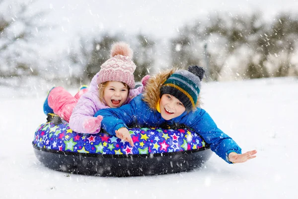 Aktives Kleinkind und Schulkind rutschen gemeinsam auf Schneeröhre den Hügel hinunter. Glückliche Kinder, Geschwister, die sich im Winter draußen auf dem Schlitten vergnügen. Bruder und Schwester auf schneebedeckter Abfahrt, Familienzeit. — Stockfoto