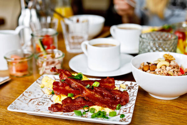 Стол накрыт на завтрак летом с различными джемом, хлебом, кофе, круассанами, яйцами, мюсли с беконом и апельсиновым соком