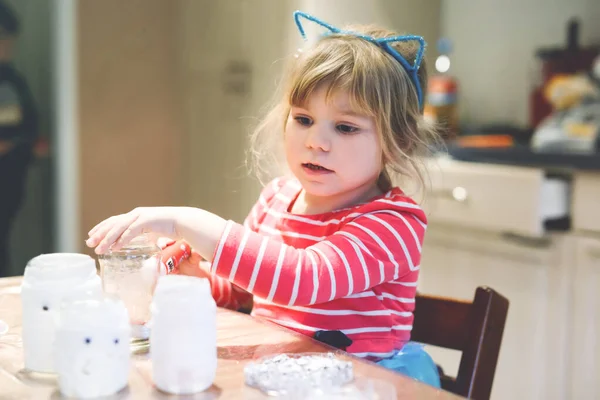 Una bambina che fa lanterne fantasma per la festa di Halloween. Bambino in età prescolare carino che fa artigianato, lanterne a lume di candela fatte da sé per la decorazione per la celebrazione del festival autunnale. — Foto Stock