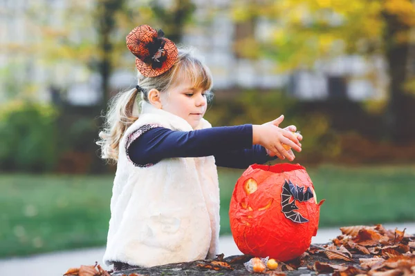 Mała dziewczynka przebrana za sztuczkę czarownicy lub psikusa na Halloween. Szczęśliwe dziecko na świeżym powietrzu, w pomarańczowym śmiesznym kapeluszu i torbie z dynią do słodkiego nawiedzenia. Rodzinny festiwal w październiku. Aktywność na zewnątrz — Zdjęcie stockowe