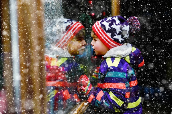 Menino da escola saudável bonito pouco no mercado de Natal. Criança feliz engraçada na moda roupas de inverno fazendo compras de janela decoradas com presentes, árvore de xmas. Neve a cair, neve a cair — Fotografia de Stock