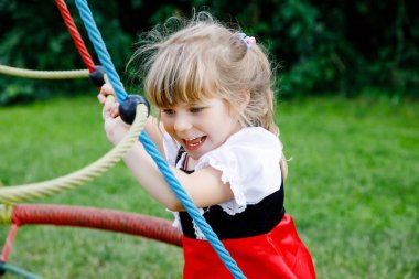 Küçük anaokulu kızı dışarıda oyun oynuyor. Çocuk tırmanışta ve yaz aylarında açık havada eğlenirken mutlu..
