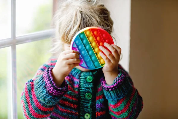 Little blonde preschool girl playing with new trend sensory toy - rainbow pop it. Antistress toy for children and adult. Colorful toy simple dimple. Squishy soft bubble toys rainbow color. Happy child — Stock Photo, Image