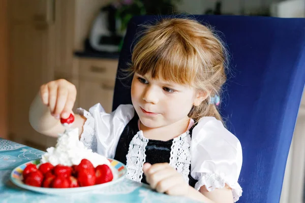 Kleine Vorschulmädchen essen frische Erdbeeren mit Schlagsahne. entzückende Baby Kind Verkostung und Beißen reife Erdbeere. gesunde Ernährung, Kindheit und Entwicklung. — Stockfoto