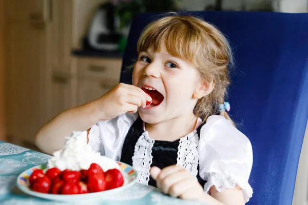 Little preschool toddler girl eating fresh strawberries with whipped cream. Adorable baby child tasting and biting ripe strawberry. Healthy food, childhood and development. — ストック写真